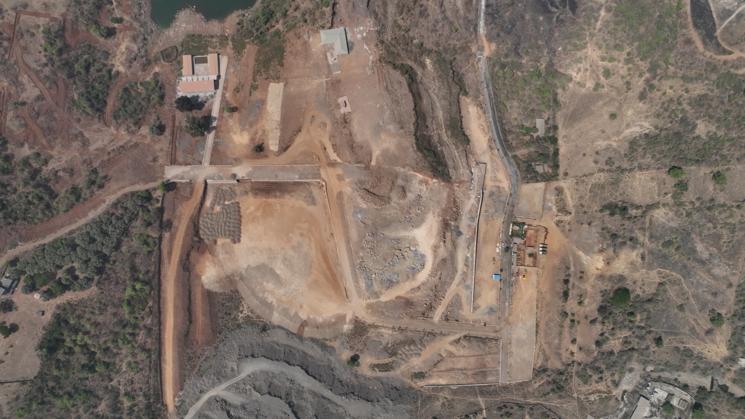 Top-down aerial photograph of the project land showing the levelled plateau, internal earthworks, retaining walls and site structures, with the lake at the top edge.